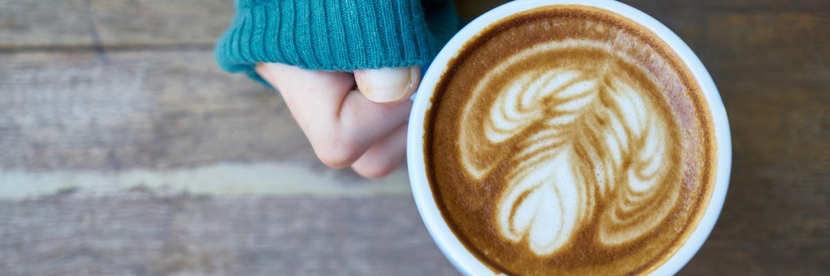 Une main tenant un café latté avec un dessin de coeur dans le lait.