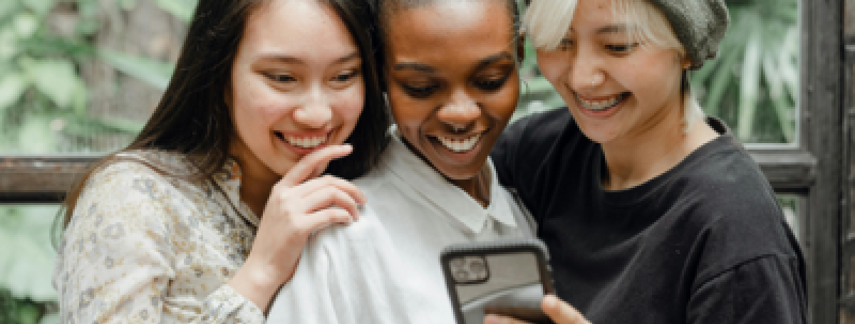 Trois jeunes femmes sur un téléphone cellulaire sourient.