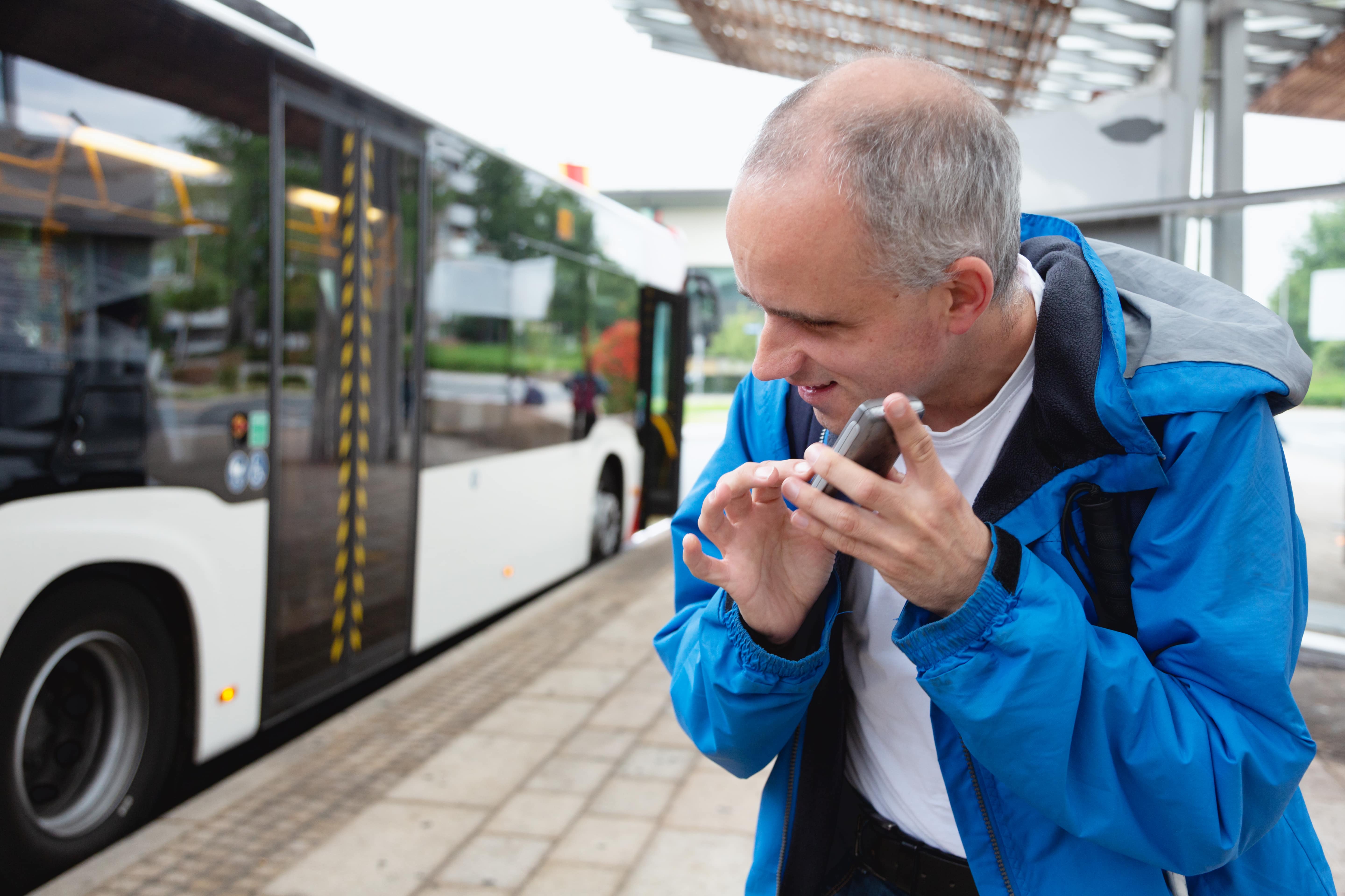 Un homme se tient près d’un autobus et touche son téléphone portable en l’écoutant.