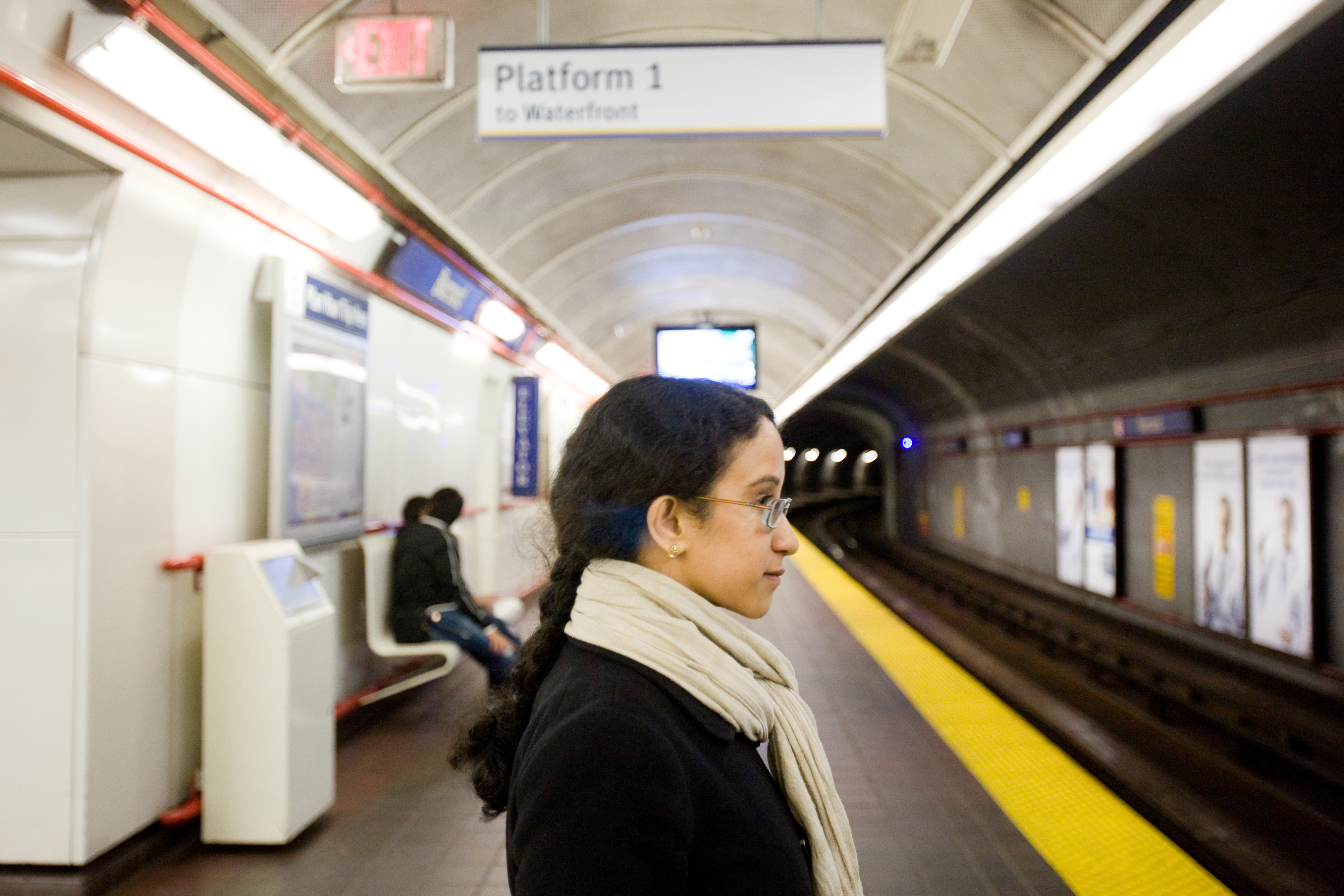 Une femme portant des lunettes attend un train sur le quai d’un métro.