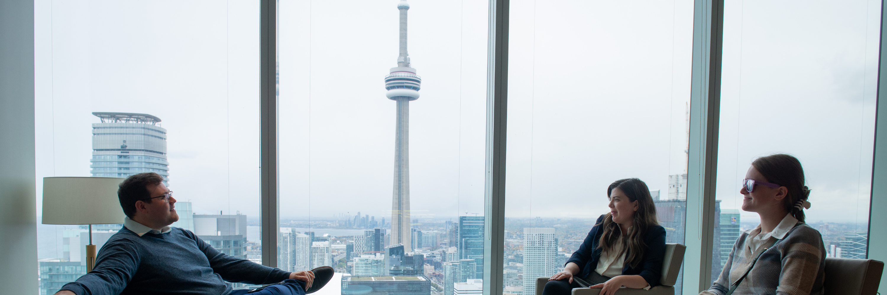 three people sit in an office with the Toronto skyline behind them.