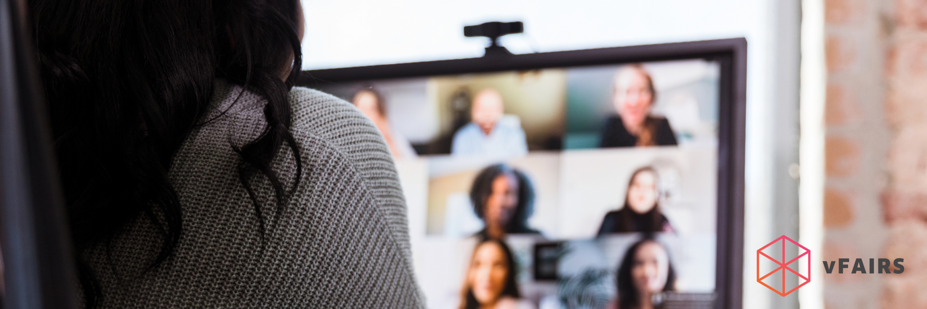 A woman sits in front of a computer screen. Several people have joined the virtual meeting. The VFairs logo appears in the bottom right hand corner.