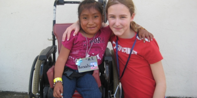 Au Guatemala, une jeune Veronika s'accroupit à côté d'une jeune fille en fauteuil roulant. Elles se tiennent par le bras et posent pour la photo.