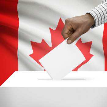 Une personne déposant son bulletin de vote dans une urne. On voit un drapeau canadien en arrière-plan.