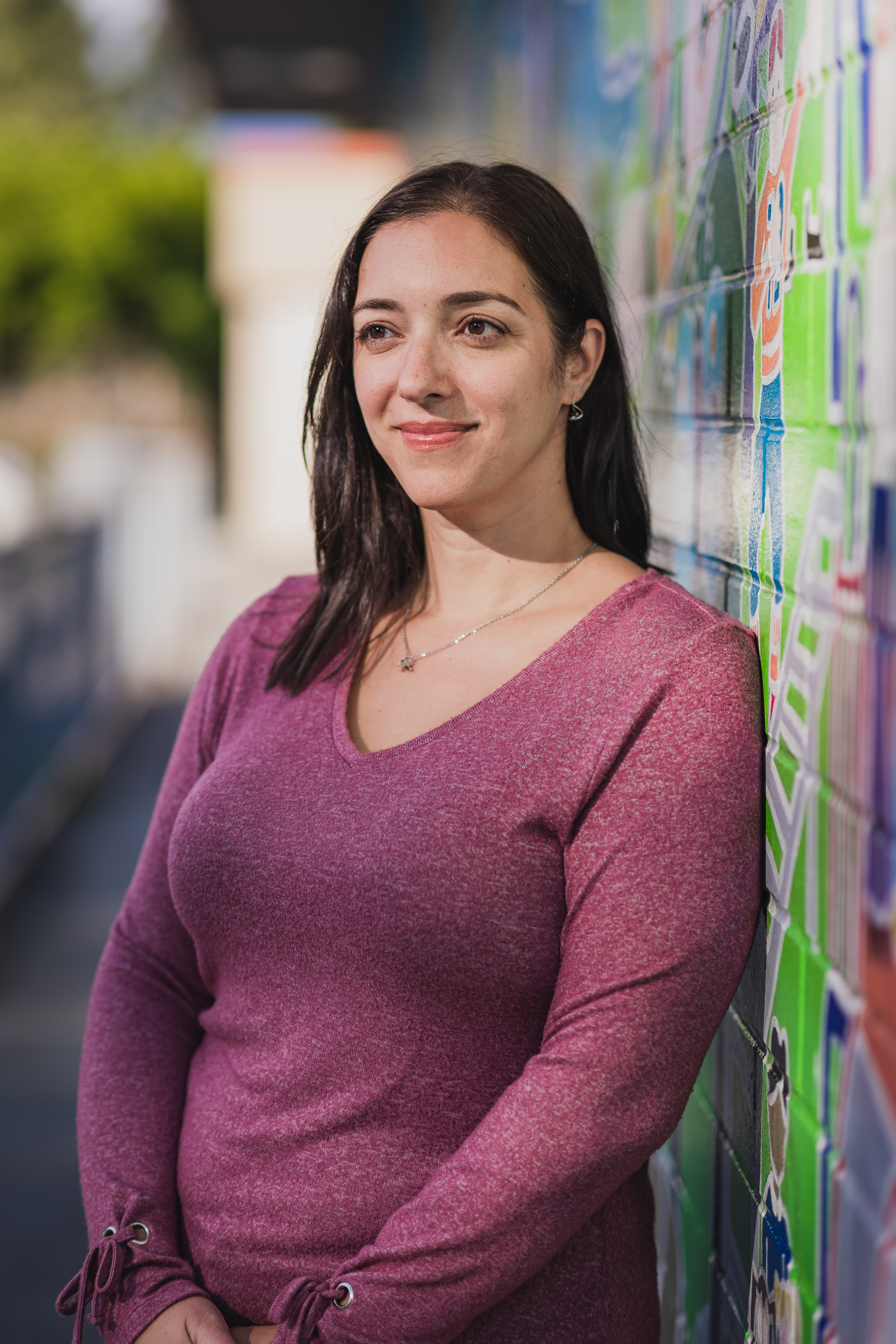 Une photo-portrait de Stefanie Volpe à côté d'un mur rempli de graffitis colorés. 