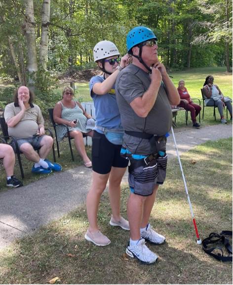 Un membre du personnel aide à fixer le casque d'un invité au pied de la tour d'escalade du camp. 