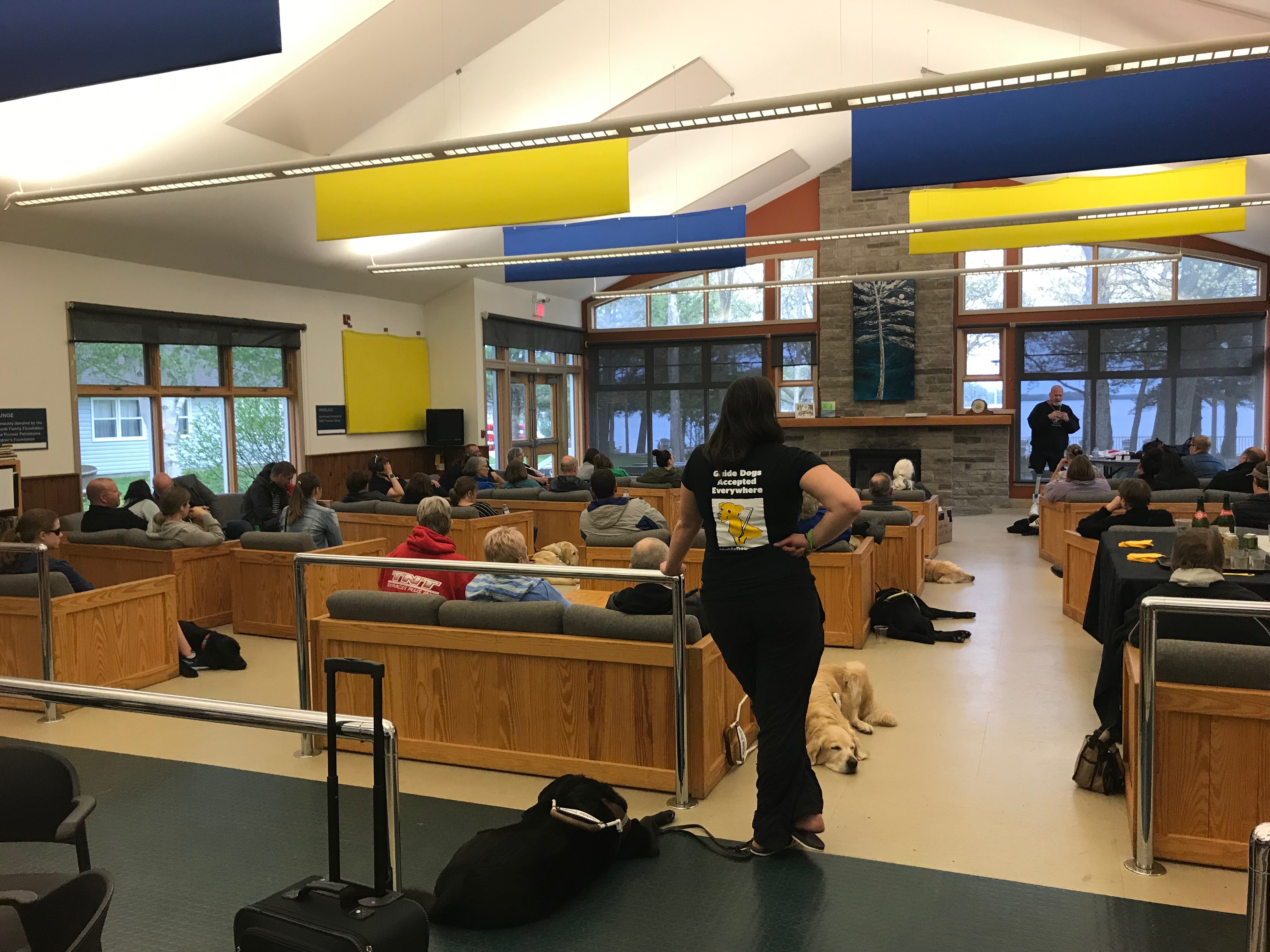 A room at Lake Joe filled with participants sitting on couches. On the floor, their guide dogs sit next to them. 