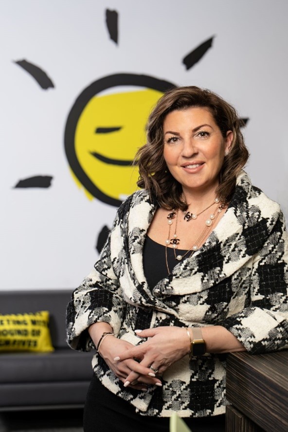 A smiling Angela Bonfanti stands in front of CNIB iconography showing a bright yellow sun