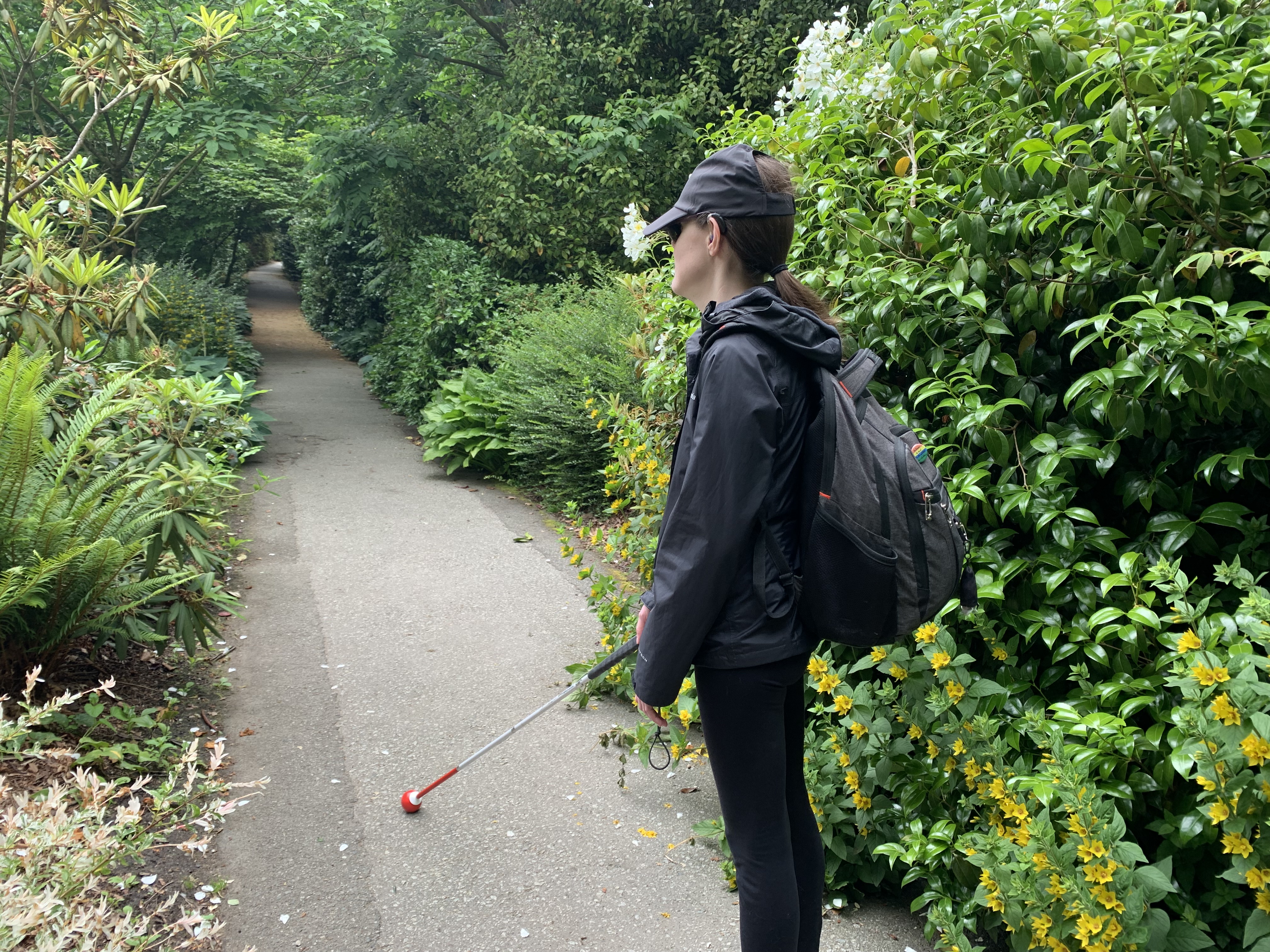 Abby marche le long d'un sentier verdoyant et s'oriente à l'aide de sa canne blanche. Abby se détourne de la caméra