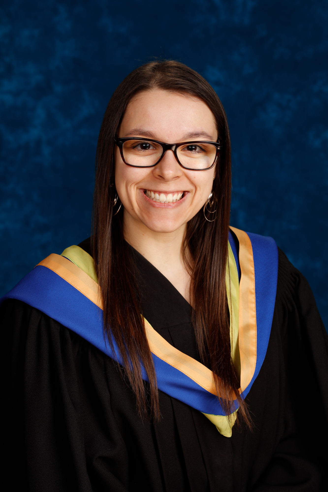 Une photo de Danica Frappier lors de la remise des diplômes. Elle est souriante et porte une robe de graduation avec une étole aux accents bleus, jaunes et dorés.