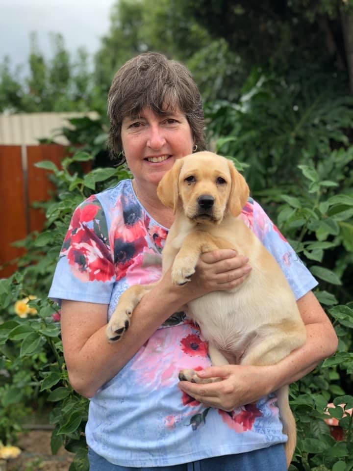 Eileen holds an 8-week-old Bridget. They stand outside against a lush green garden.