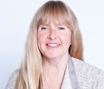 Un portrait professionnel de Diane Bergeron.  Elle est souriante, assise devant un fond blanc, et porte un cardigan gris et blanc. 