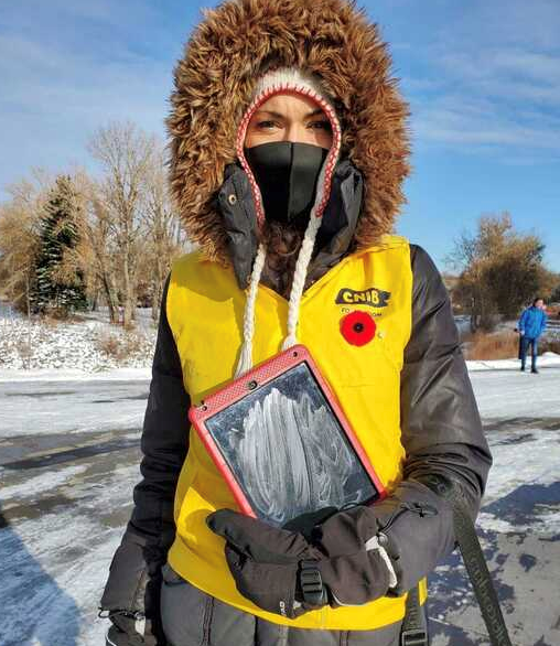 Un collecteur de fonds d’INCA vêtu d'une parka et d'un gilet jaune vif, portant un masque et tenant une tablette.