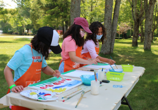 Three girls at a table outside doing arts & crafts.