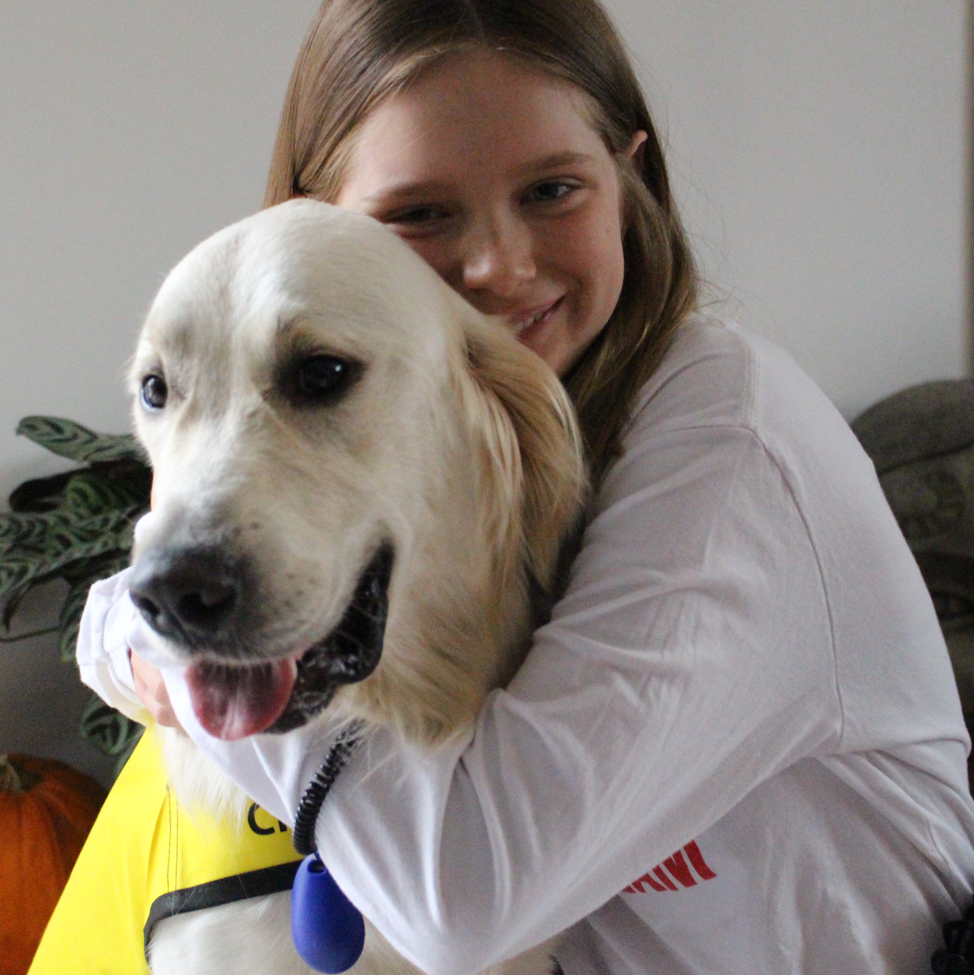 Dani assise et serrant dans ses bras son chien George, un Golden Retriever portant le gilet jaune vif des chiens compagnon d'INCA, tous deux souriant pour la prise de photo