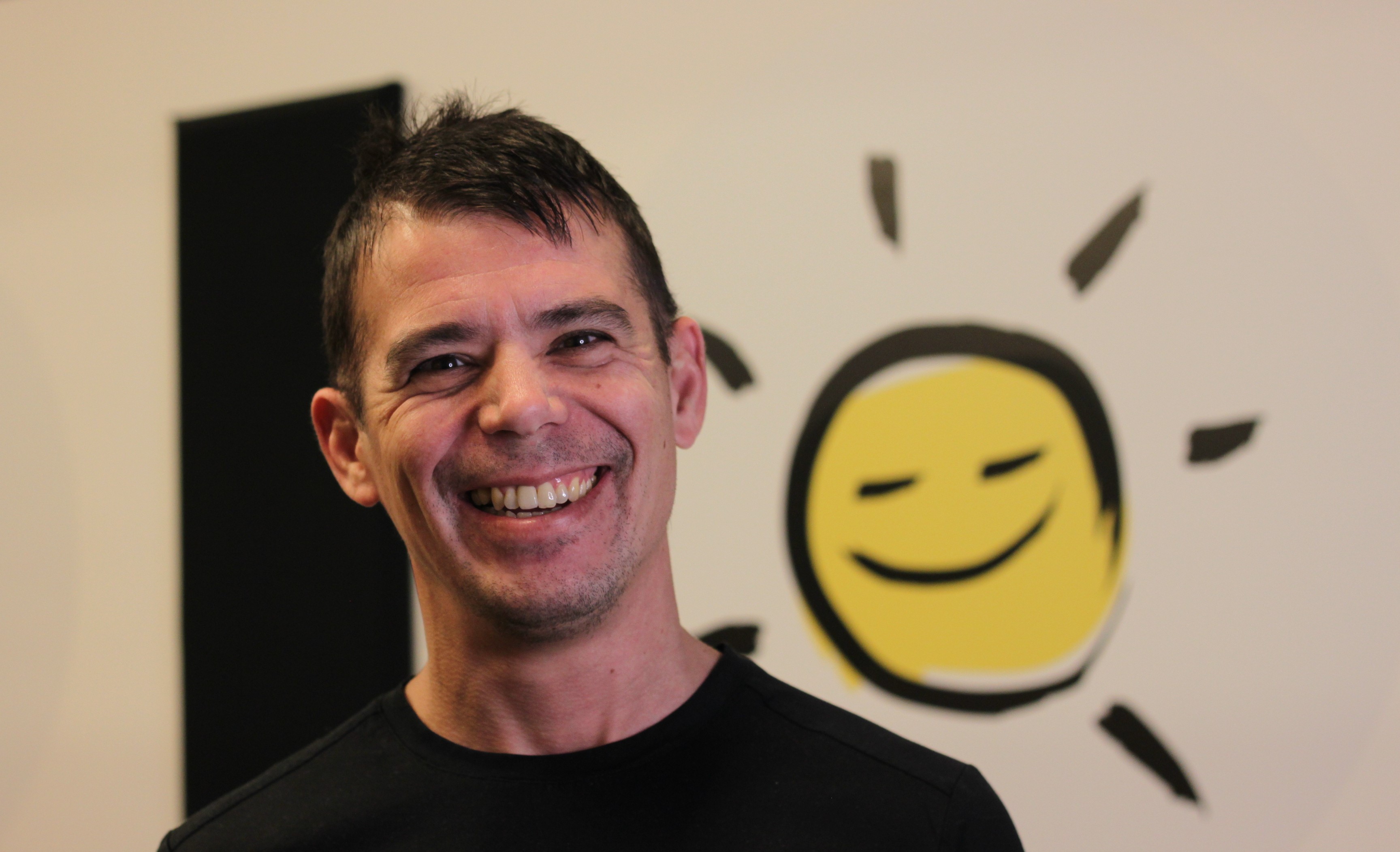 David sourit. Sur le mur derrière lui, l'icône des programmes Vivre d'INCA (un soleil jaune souriant aux couleurs d'INCA).
