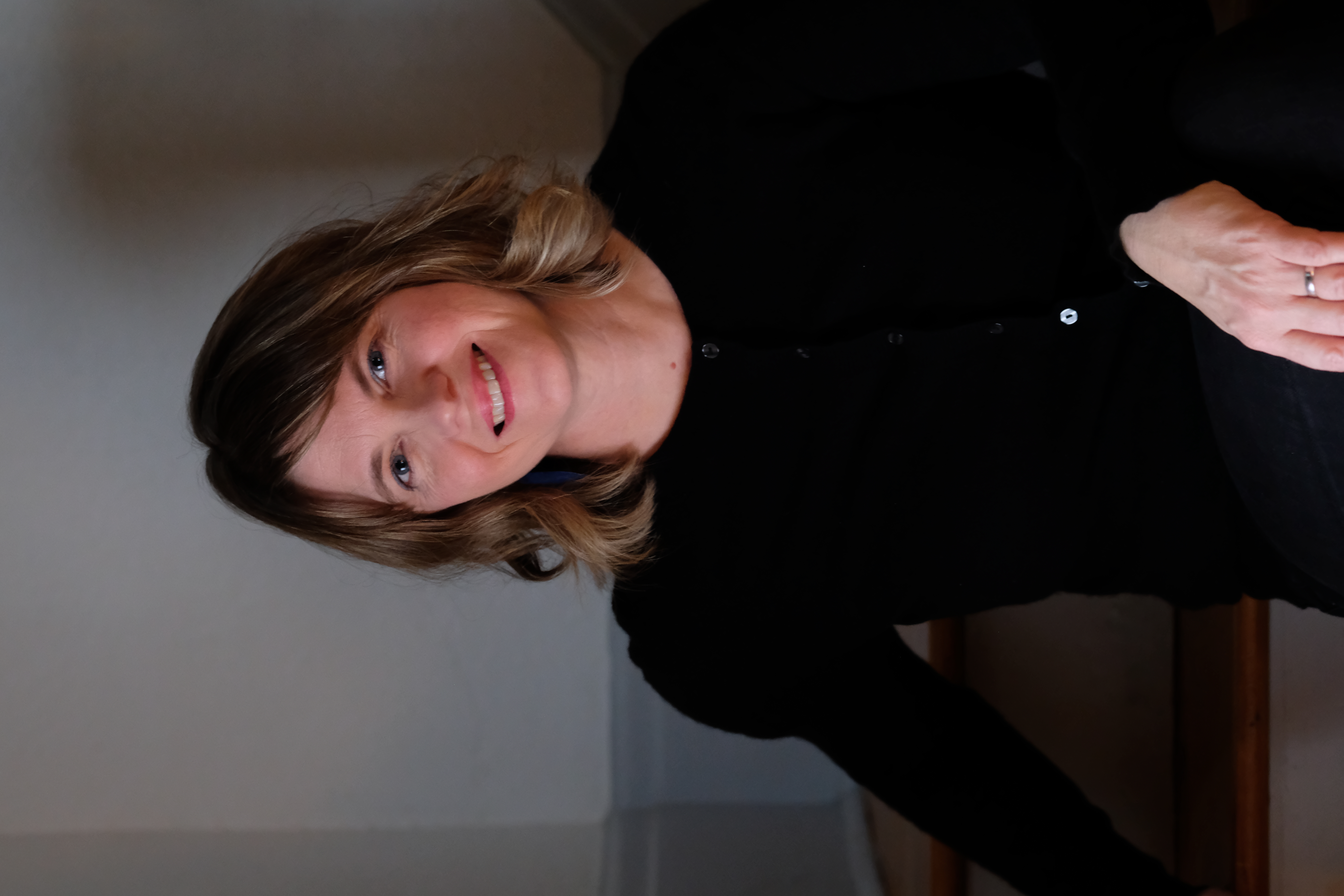 A professional headshot of Emily Urquhart. Emily is wearing a black long-sleeve shirt and has medium length brown hair and a smiling facial expression. 