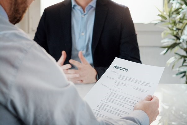 A job interview. An employer holds a resume. In front of him is someone being interviewed.