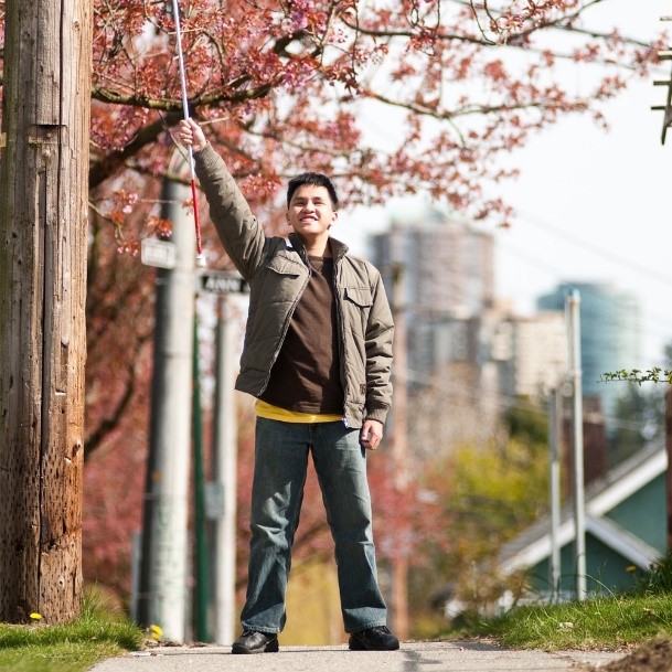 A young man holds his white cane in the air triumphantly.  