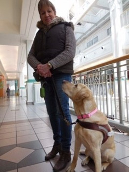 Sharon Ruttan debout avec son chien guide, Hominy, assise et la regardant.