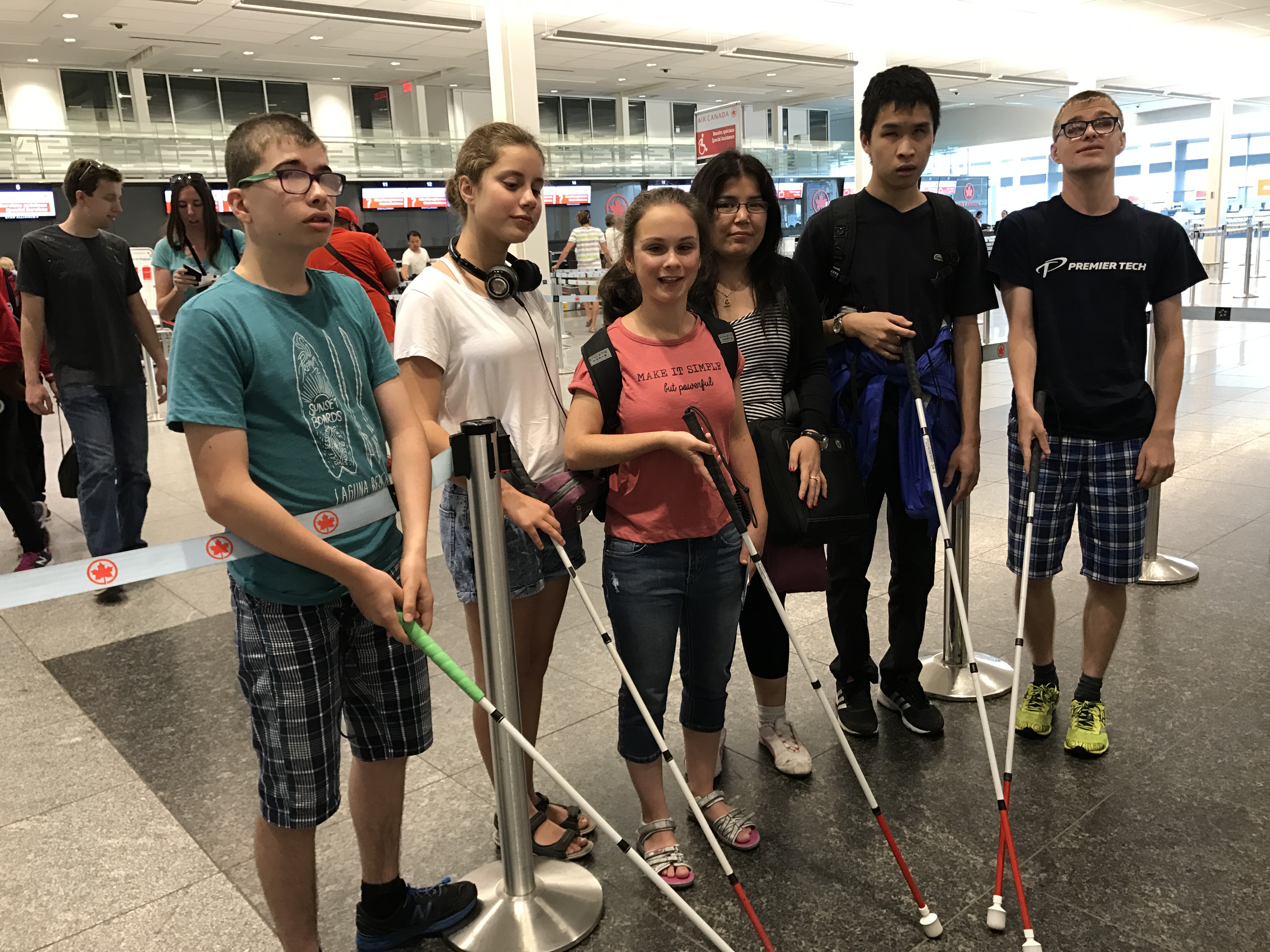 Cinq jeunes à l'aéroport joignent leur canne blanche ensemble.