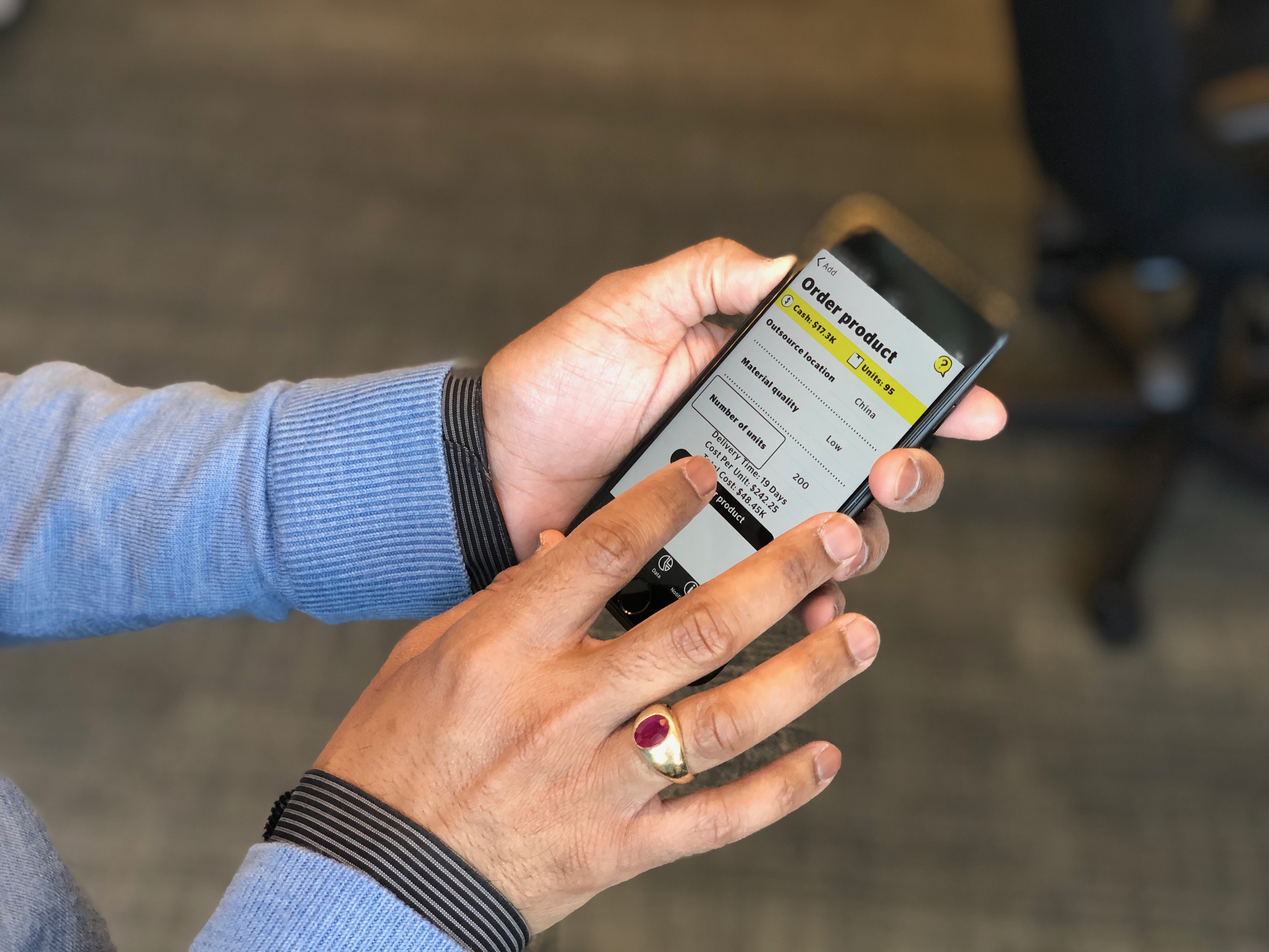 A close-up of a man's hands holding an iPhone and playing the Venture Zone game.