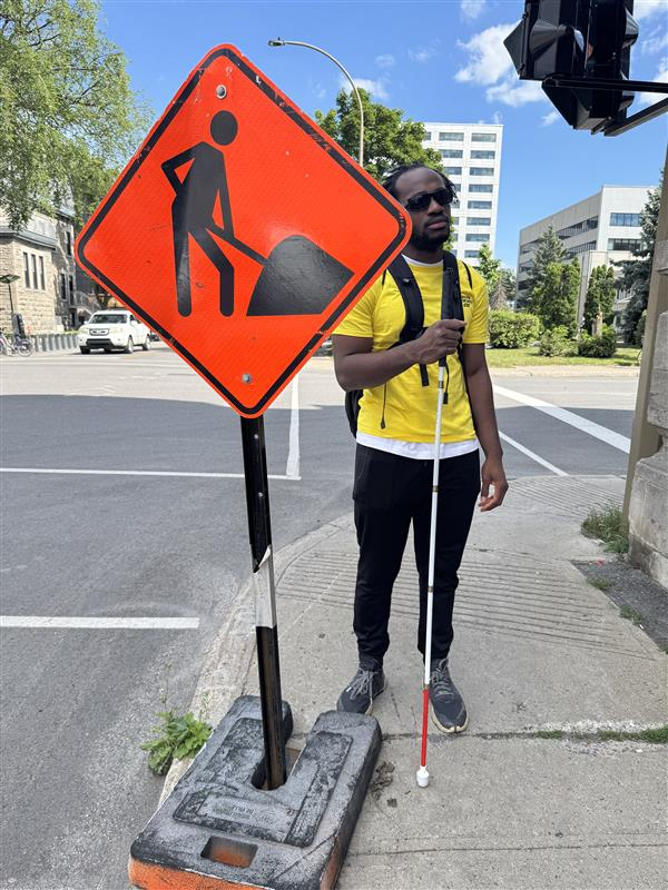 Une personne derrière un panneau de travaux orange plus large que la base et qui arrive de son visage.