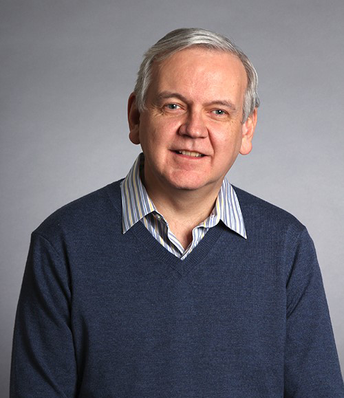 Photo de Jim Maher assis devant un fond gris. 