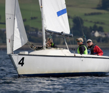 Joshua Cook et deux autres personnes sont assises dans un bateau à voile sur l'eau. Ils sont aux championnats du monde de voile aveugle en Ecosse.