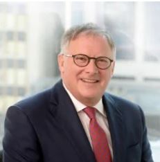 A professional headshot of Ken Fredeen. He is wearing a suit and smiling.