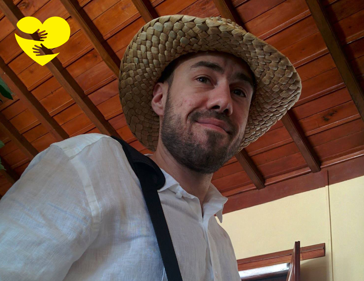 Kevin, coiffé d’un chapeau de paille et sourit pour la photo. Un dessin de bras serrant un cœur jaune illustré se trouve dans le coin supérieur gauche de la photo.