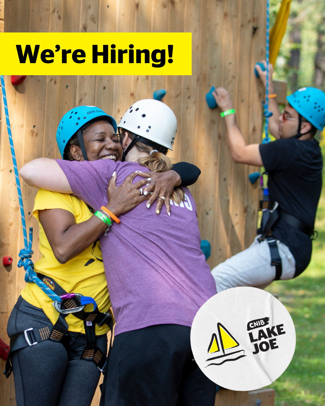 A woman wearing rock climbing equipment gives a staff member a big hug after finishing her climb. She has a huge smile on her face. The text, “We’re Hiring” and a white sticker with the CNIB Lake Joe logo