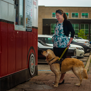 Une femme avec un golden retriever portant un harnais jaune devant un camion de cuisine de rue.