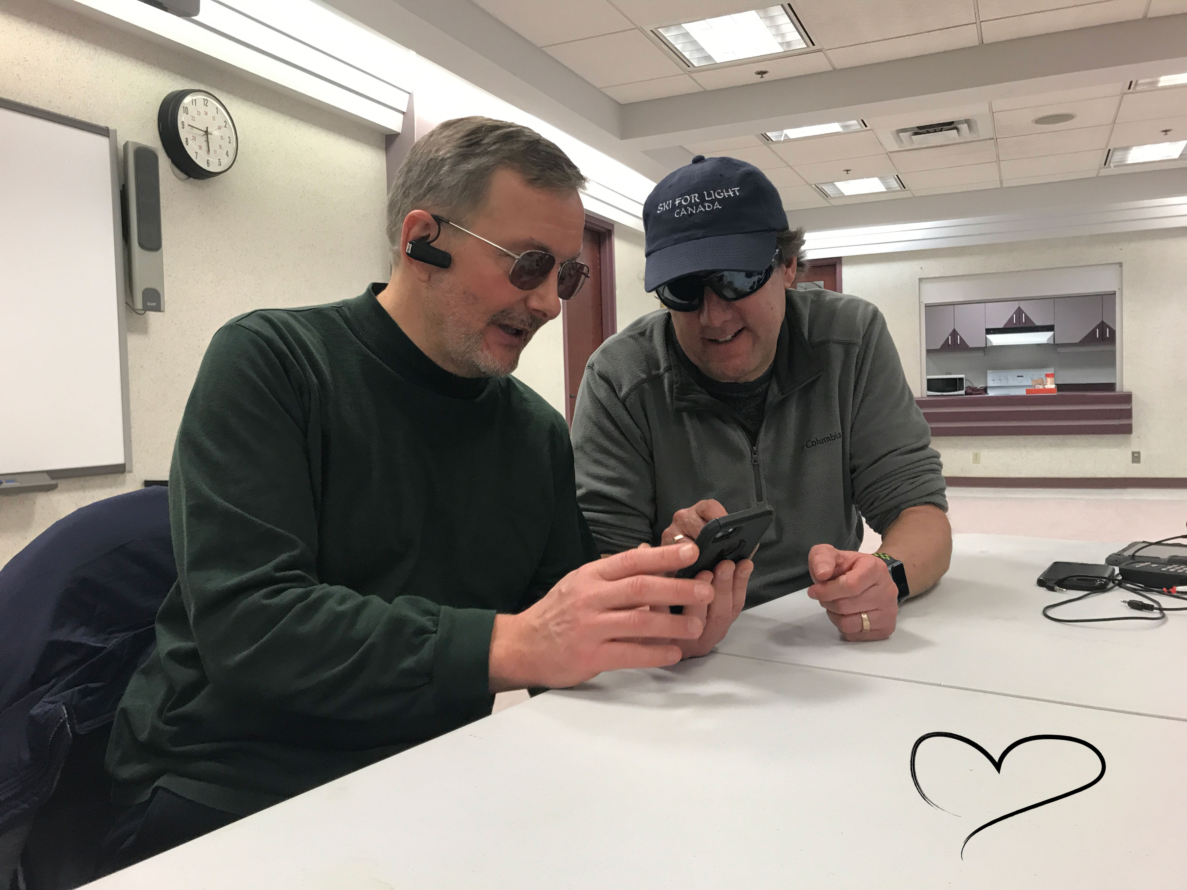 Lloyd Buckler, sitting down at a table helping someone learn how to navigate their iPhone. 