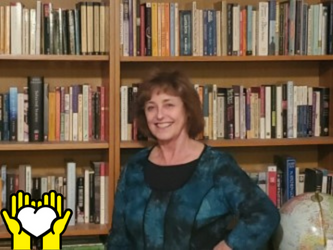 Une photo de Lynn Kennedy posant en face d'une étagère de livres.  L'icône de deux mains tenant un cœur blanc sur un fond jaune, dans le coin inférieur gauche.