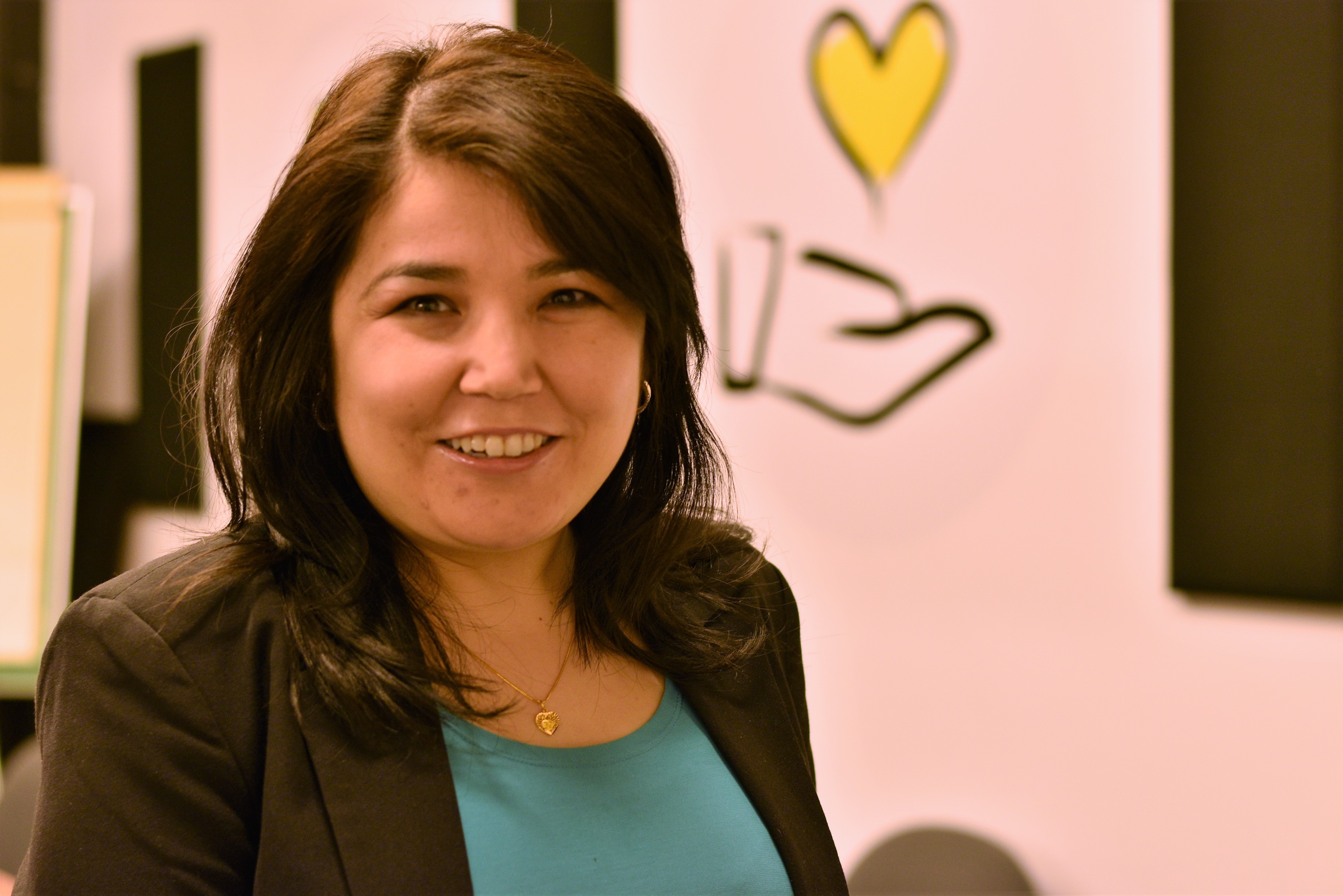 Najla sourit. Derrière elle l'icone d'une main qui tient un coeur jaune.