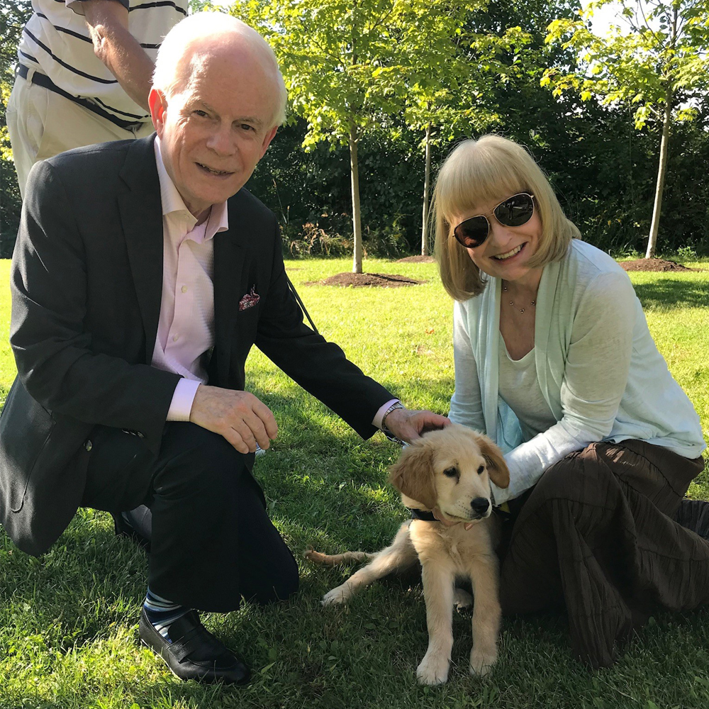 Un homme et une femme souriant et un chiot Golden Retriever allongé sur l'herbe.