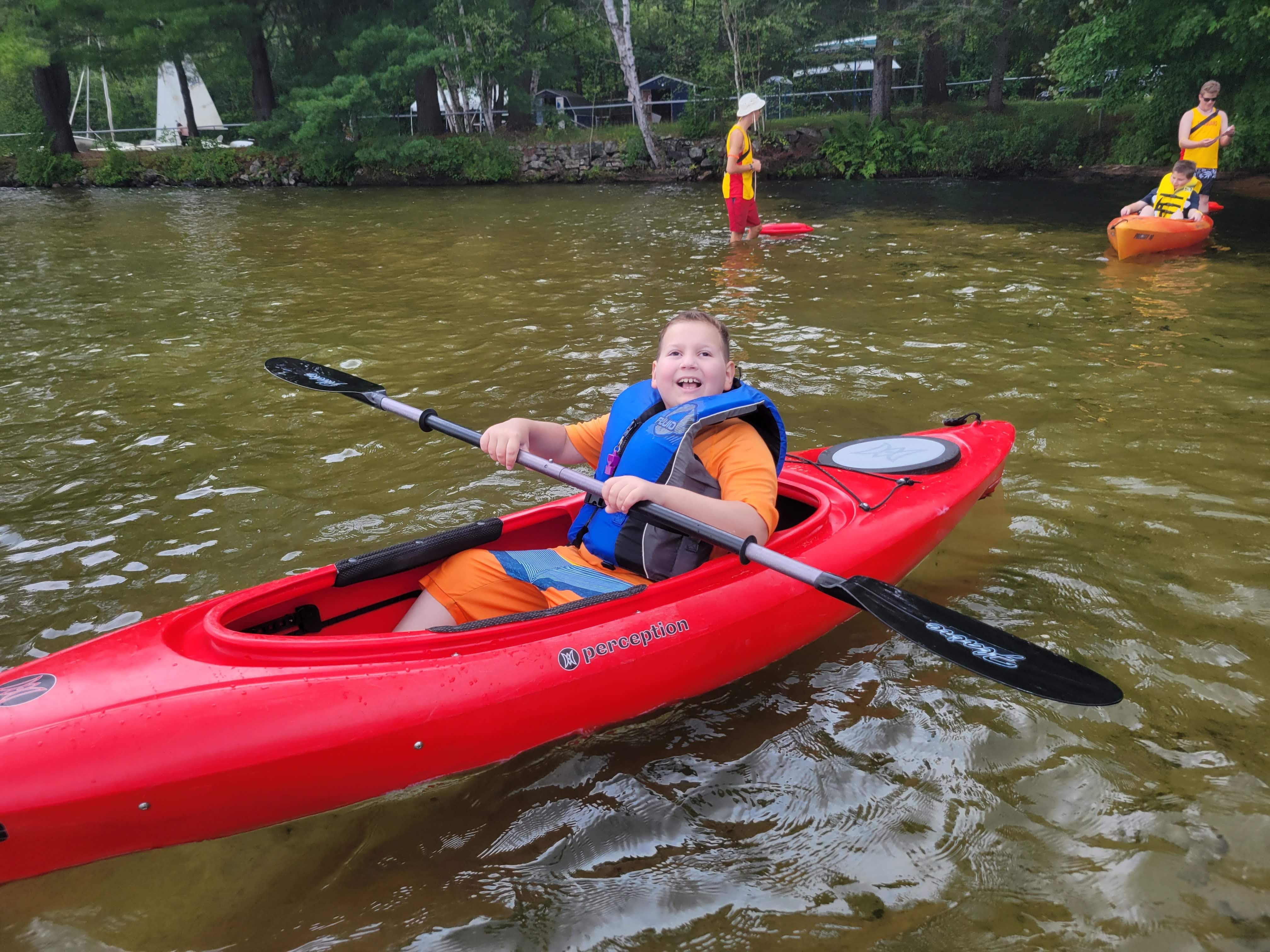 Ollie est assis dans un kayak rouge sur le lac au camp Lake Joe d’INCA