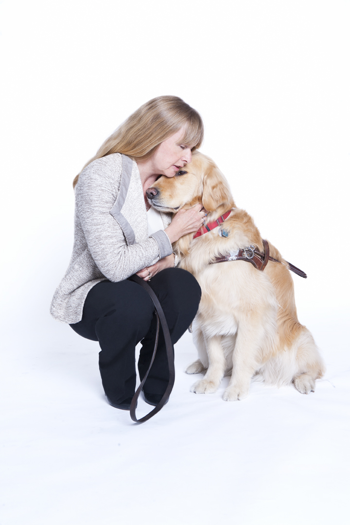 Diane Bergeron crouches for a photo alongside Lucy. Lucy's head is resting on Diane's shoulder. Diane is lovingly petting her. 