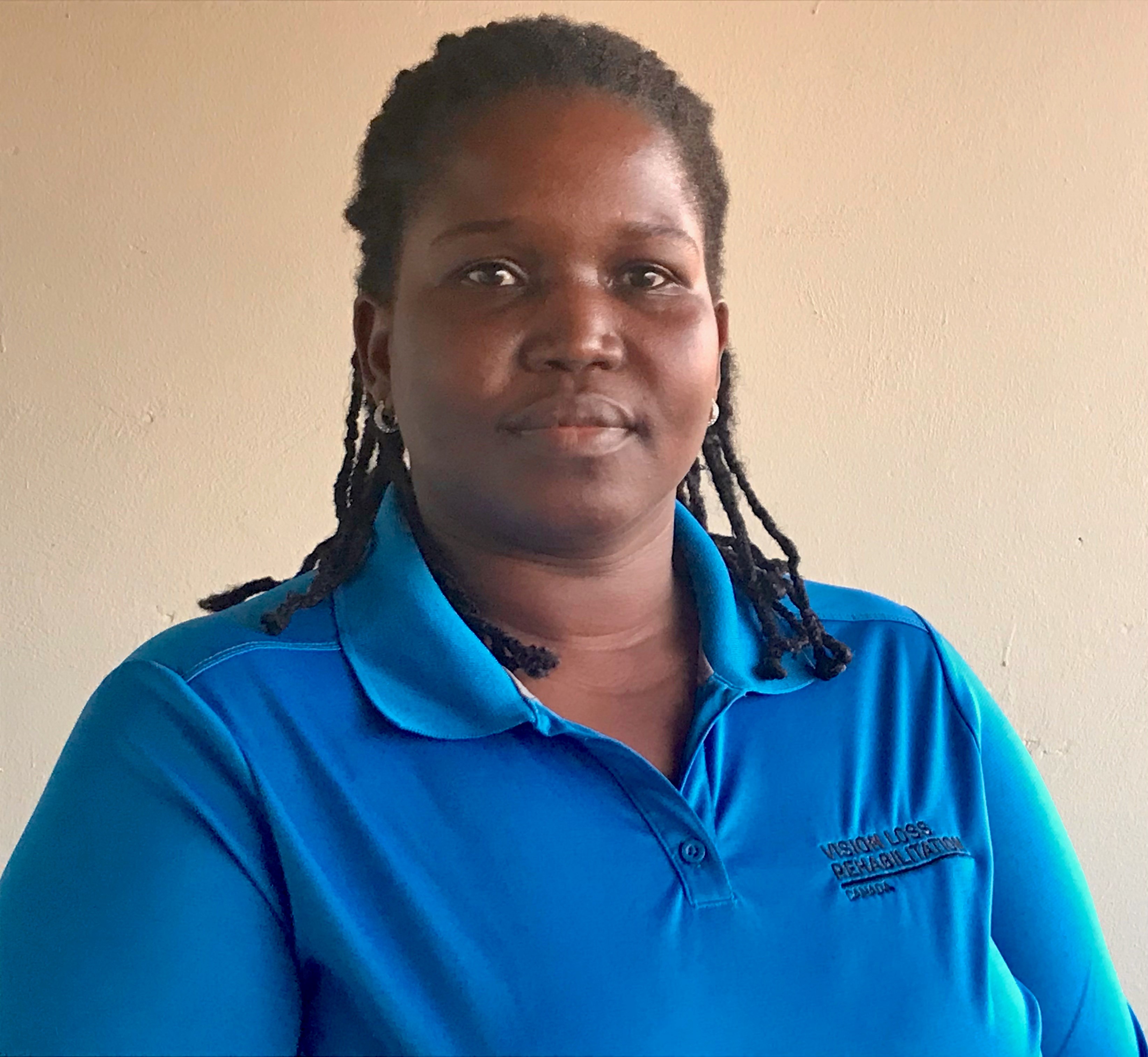 A professional headshot of Irene. She has braided hair and is wearing blue Vision Loss Rehabilitation Canada polo shirt.