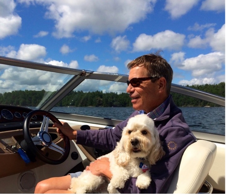 Randall Oliphant is driving a boat with a dog on his lap.