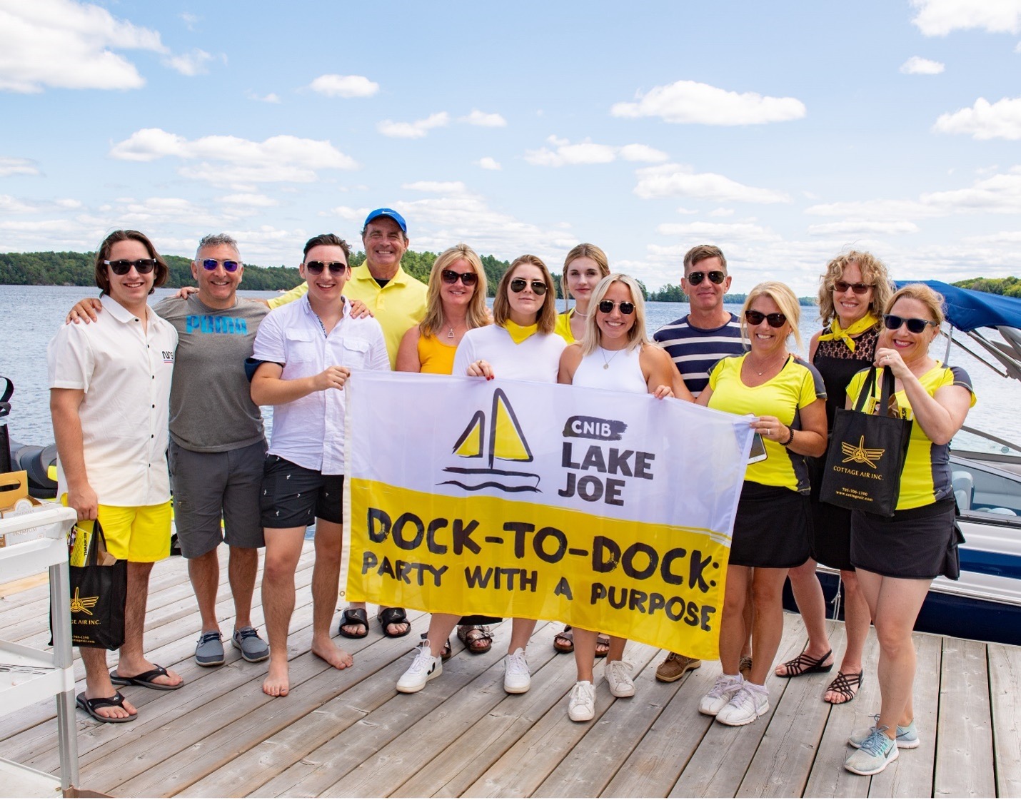 Un groupe de bénévoles de l’événement sur le quai du centre Lake Joseph d’INCA tient un drapeau « De quai en quai » une fête pour une bonne cause d’INCA » 