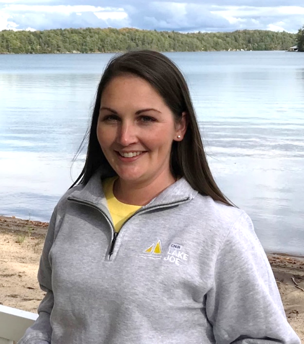 Lindsay Garrett, Program Manager, is standing on the Lake Joe beach modelling a gray quarter zip sweatshirt.