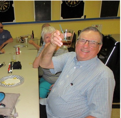 Wayne Laffin, sitting at a table with fellow guests at Legion Night at the Legion in MacTier, raising his glass with a big smile.