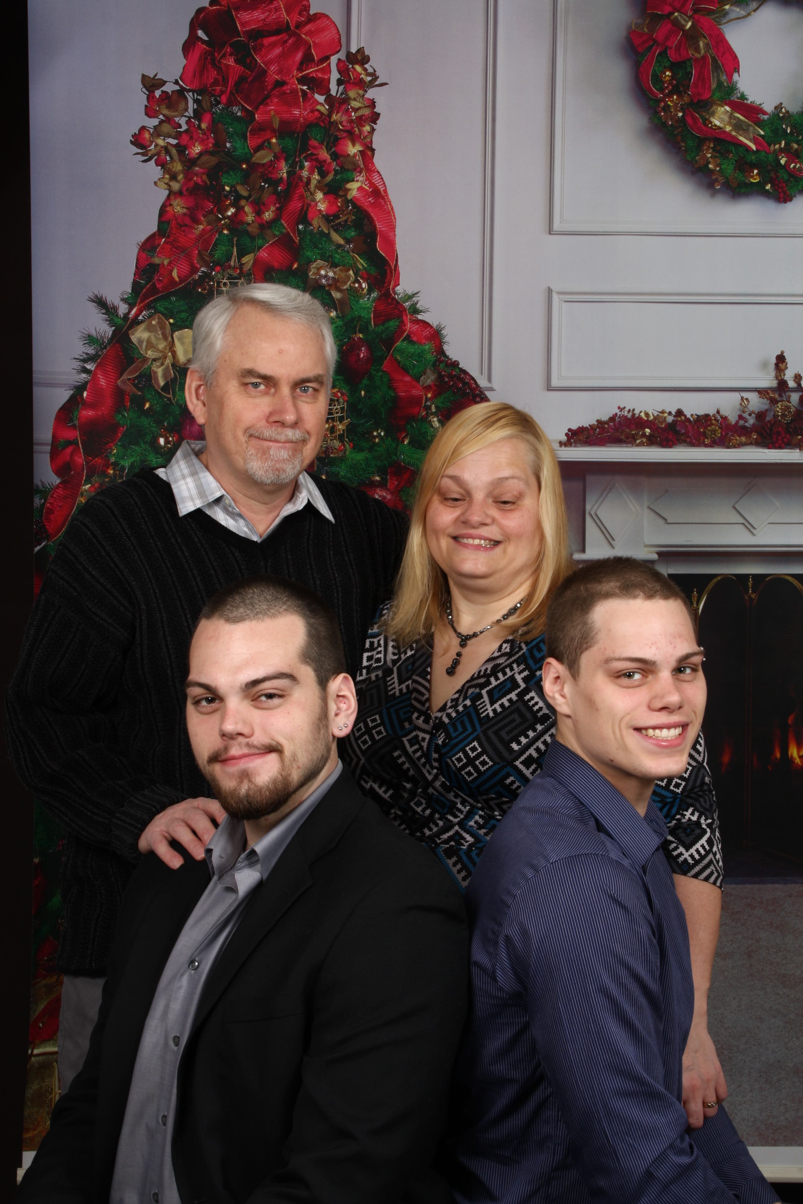 Une photo de famille sur une carte de Noël. Rhonda, son mari et ses deux garçons adultes font la pose. Un arbre et une couronne de Noël se trouvent en arrière-plan. 