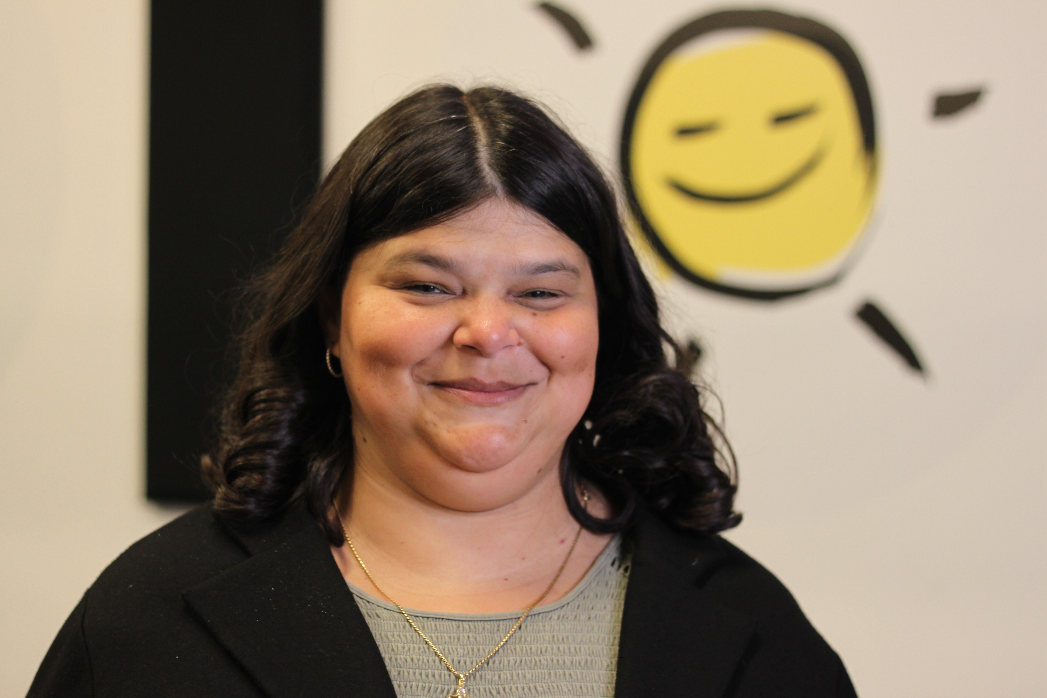 Photo de Rosie en face de l'icône en forme de soleil souriant aux couleur jaune et noir d'INCA.