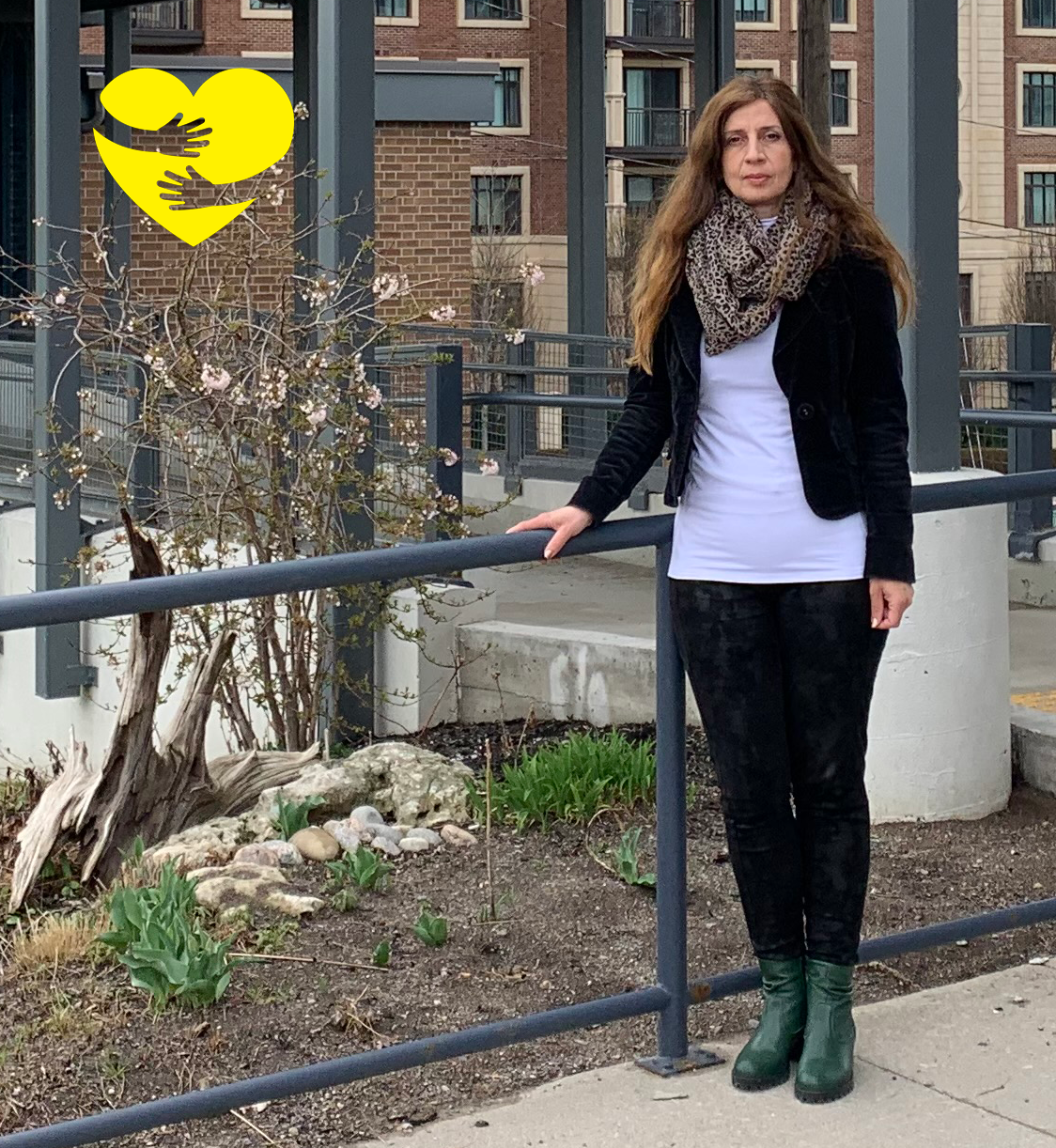 Rositsa, standing outside holding a railing. A graphic of arms hugging a yellow cartoon heart can be found in the top left corner.