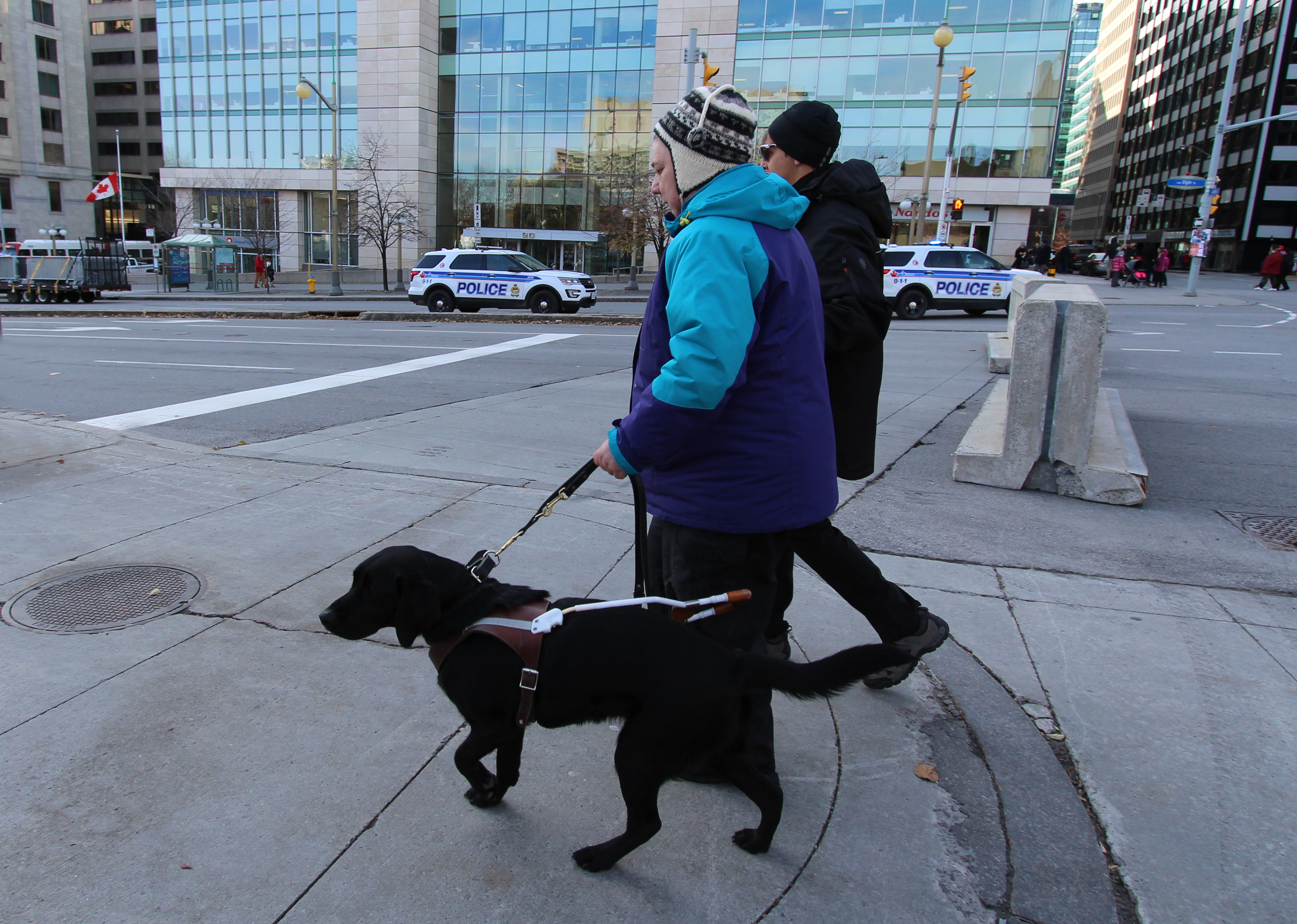 Sandy et de son chien-guide Keller, marchant sur un trottoir dans un quartier animé du centre-ville par une journée froide.