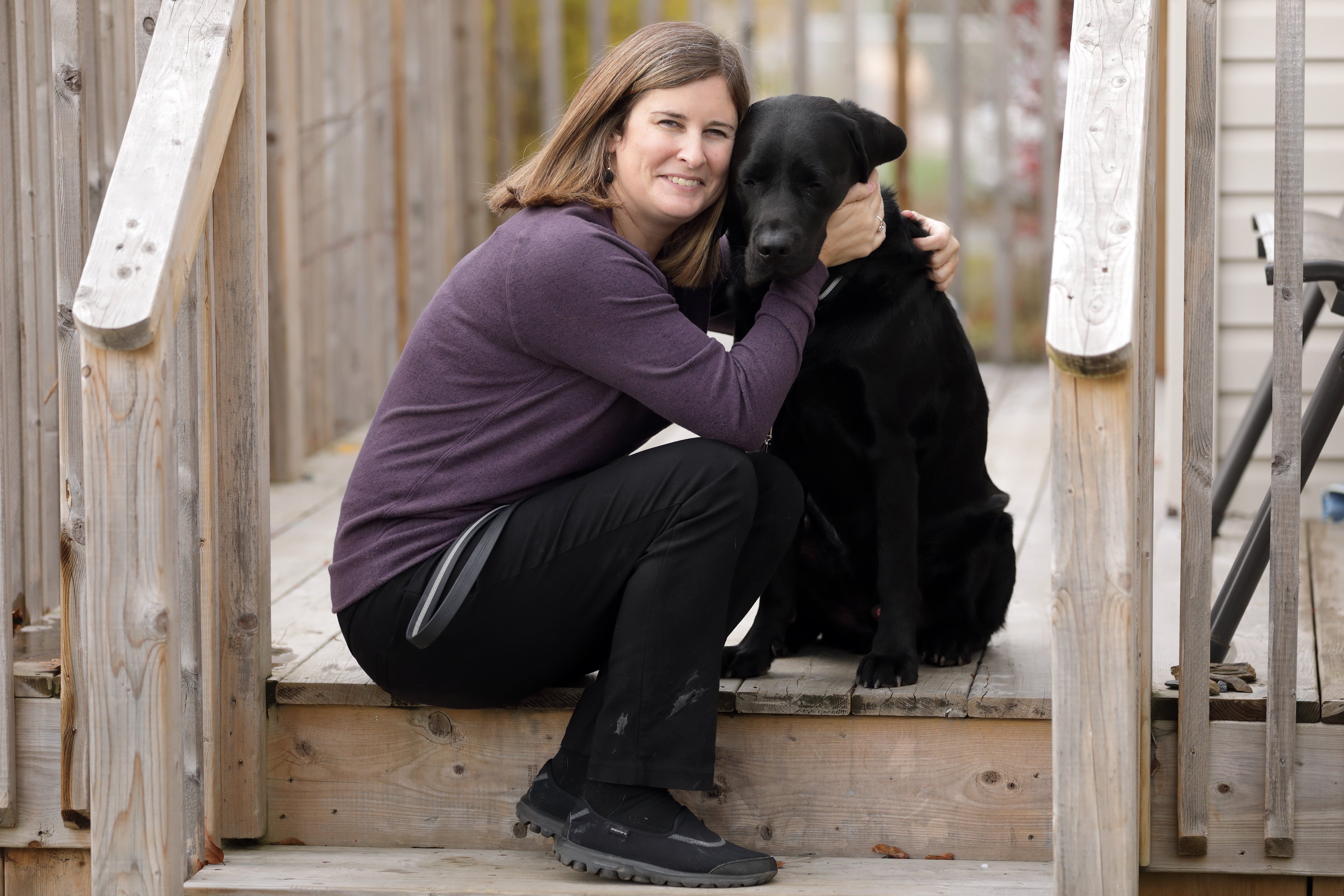 Photo de Shelley assise sur un perron en bois, souriant et donnant un gros câlin à Rookie. 