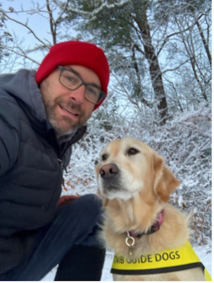 Barry kneeling outside in the snow beside Willow wearing her CNIB Guide Dogs vest.